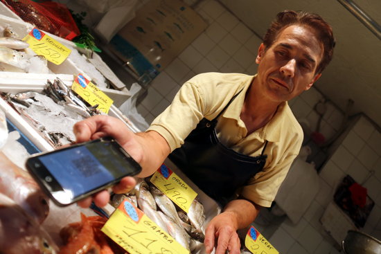 A fishmonger at the Besòs market shows the application to pay with a new digital currency on October 3 2018 (by Miquel Codolar)